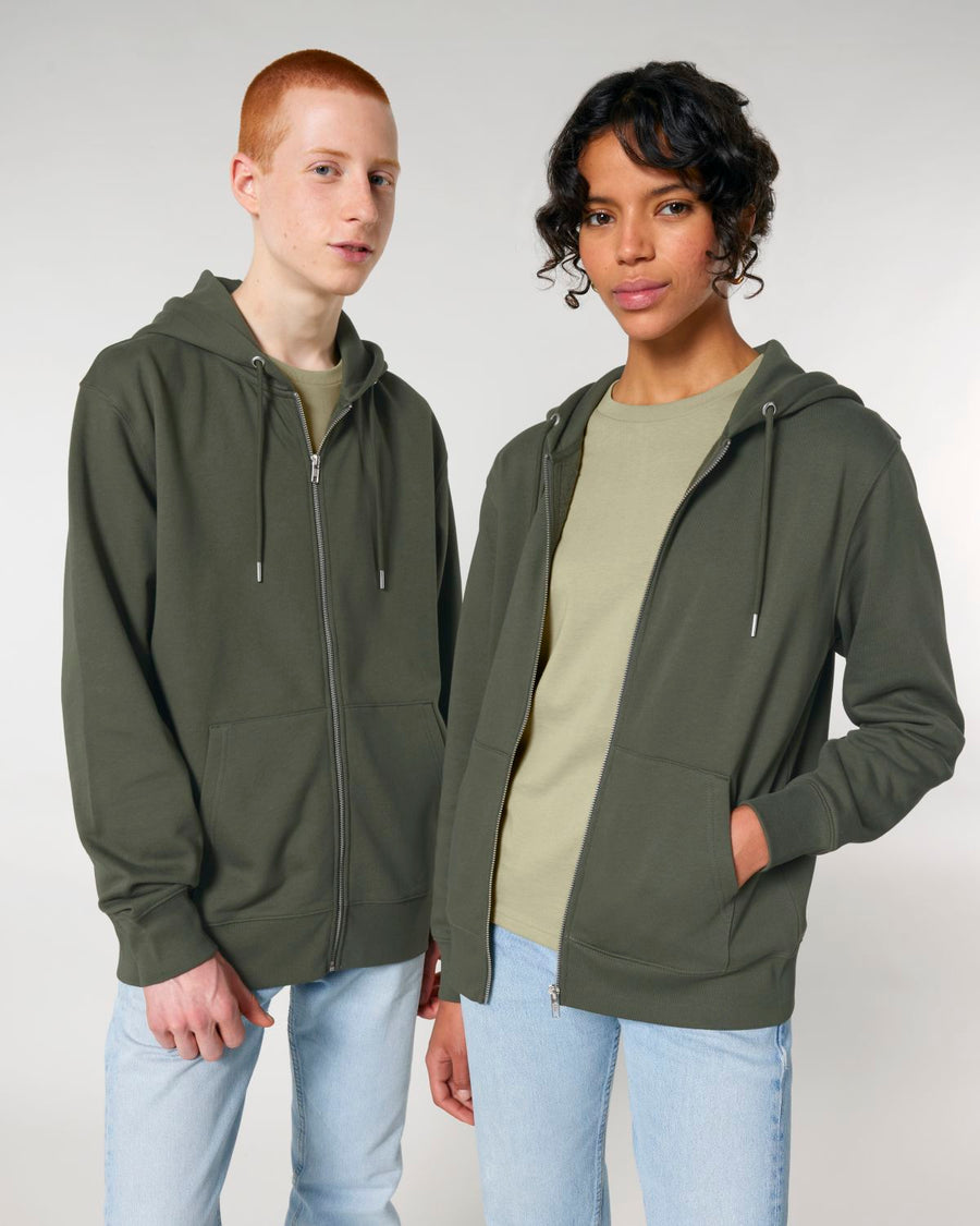 Two people wearing Stanley/Stella's STSU179 Stella/Stella Cultivator 2.0 The Iconic Unisex Zip-thru Hoodie Sweatshirt in olive green, made from soft brushed fleece, and light blue jeans stand next to each other against a plain background.