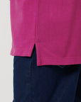 Close-up of a person wearing the Stanley/Stella STPK908 Mini Sprinter The Iconic Kids Polo in magenta with a side slit hem, paired with dark blue pants.
