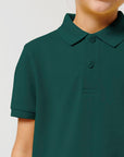 A child wears the Stanley/Stella Mini Sprinter The Iconic Kids Polo (STPK908) in dark green, shown from shoulders to mid-chest against a plain background.