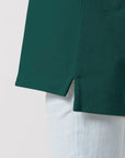 Close-up of the hem of a dark green Stanley/Stella STPK908 Mini Sprinter The Iconic Kids Polo with a side slit, worn over light-colored pants.