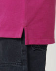 Close-up of the hem of the Stanley/Stella STPK908 Mini Sprinter The Iconic Kids Polo in magenta piqué, featuring a side slit, worn over dark denim jeans.