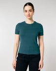 A person with tied-back hair, wearing a teal STTW174 Stella Ella Womens Fitted Loose Knit T-Shirt by Stanley/Stella and black pants, stands against a plain white background, facing forward with a neutral expression.