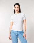 A person with long brown hair wearing a white short-sleeve STTW174 Stella Ella Womens Fitted Loose Knit T-Shirt by Stanley/Stella and blue jeans stands against a plain background.