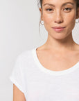 Portrait of a person with light brown hair, wearing a white Stanley/Stella STTW112 Stella Rounder Slub Rolled Sleeve T-Shirt made from organic cotton and hoop earrings, looking at the camera against a plain background.