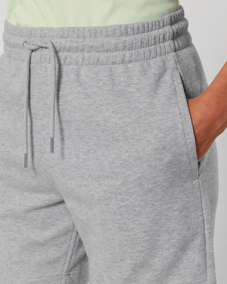 Close-up of a person wearing STBU186 Stella/Stella Trainer 2.0 The Iconic Mid-light Unisex Jogger Shorts by Stanley/Stella with hands in pockets. Made from recycled polyester and organic cotton, these unisex joggers feature a drawstring and an elastic waistband.