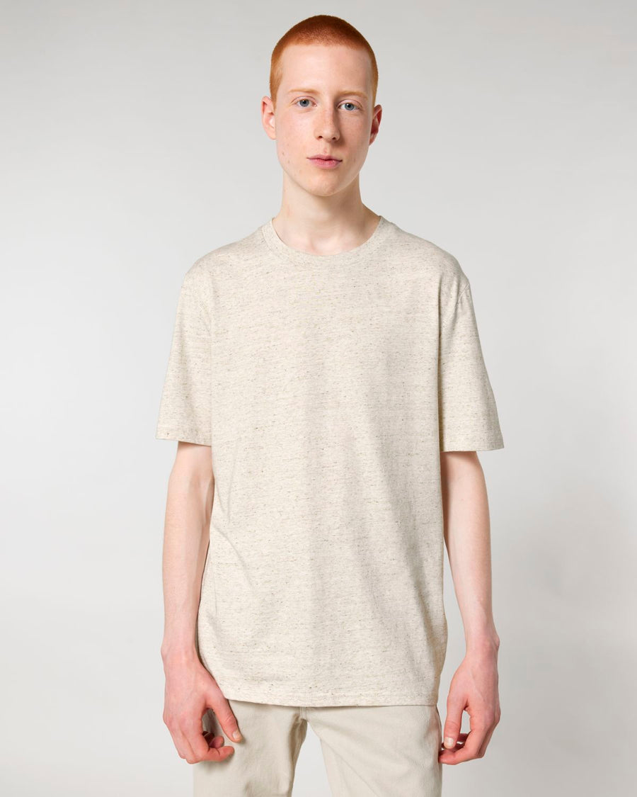 A young man wearing a Stanley/Stella Creator 2.0 The Iconic unisex t-shirt and light pants stands against a plain background.