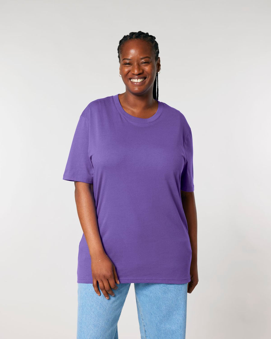Woman smiling in a Stanley/Stella Creator 2.0 The Iconic Unisex T-Shirt and jeans against a neutral background.