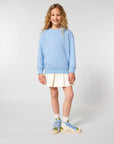 A girl wearing a Stanley/Stella organic cotton blue sweater and white skirt.