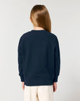The back view of a girl wearing a STSK181 Stella/Stella Mini Changer 2.0 The Iconic Kids' Crew Neck Sweatshirt in navy by Stanley/Stella.
