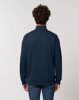 Person with curly hair wearing a dark blue, long-sleeve STSM611 Stanley Trucker Men's Quarter Zip Organic Cotton Sweatshirt by Stanley/Stella and blue jeans, facing away from the camera against a plain background.