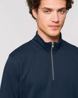 A person with short curly hair is wearing a dark blue Stanley/Stella STSM611 Stanley Trucker Men's Quarter Zip Organic Cotton Sweatshirt and looking at the camera.