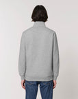A person with shoulder-length hair is seen from the back wearing a grey STSM611 Stanley Trucker Men's Quarter Zip Organic Cotton Sweatshirt by Stanley/Stella and blue jeans.