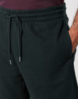 Close-up of a person wearing black STBU186 Stella/Stella Trainer 2.0 The Iconic Mid-light Unisex Jogger Shorts by Stanley/Stella and a dark shirt, with their right hand in their pocket.