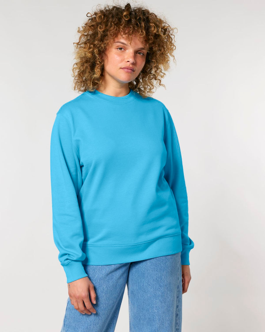 A woman with curly hair wearing a STSU178 Stella crew neck sweatshirt and blue jeans stands against a white background.