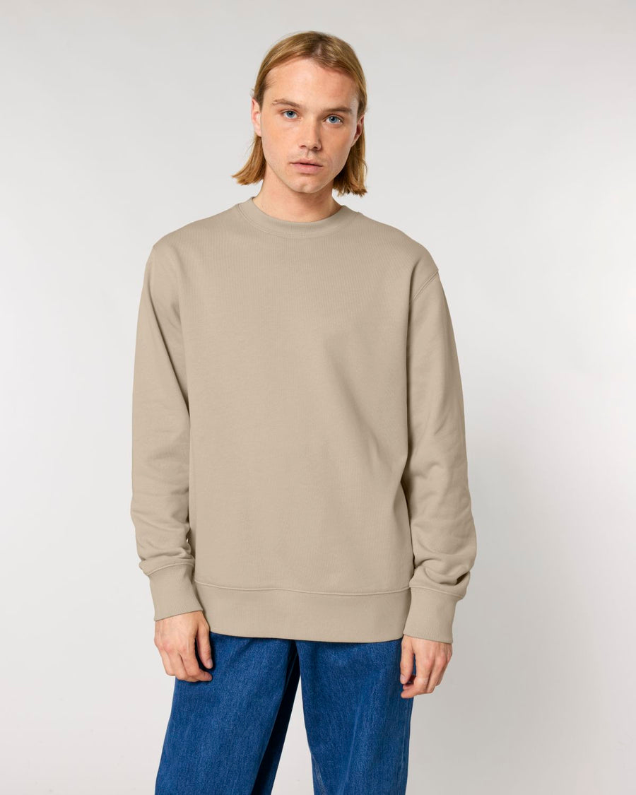 Man wearing a plain beige STSU178 Stella Changer 2.0 The Iconic Unisex Crew Neck Sweatshirt made from organic cotton and blue jeans against a white background.