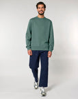 Man modeling casual outfit with green Stanley/Stella STSU178 The Iconic Unisex Crew Neck Sweatshirt and navy pants.