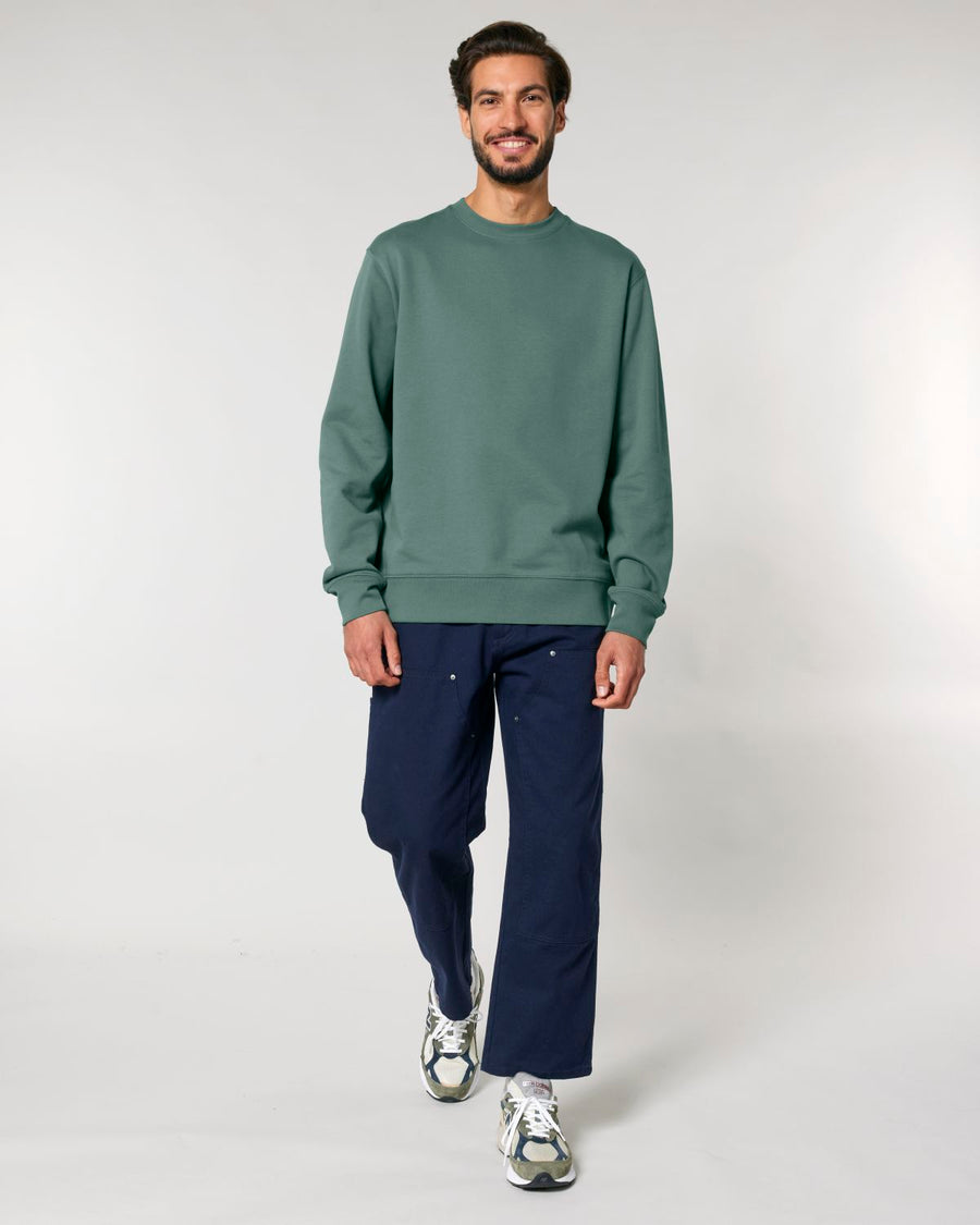 Man modeling casual outfit with green Stanley/Stella STSU178 The Iconic Unisex Crew Neck Sweatshirt and navy pants.