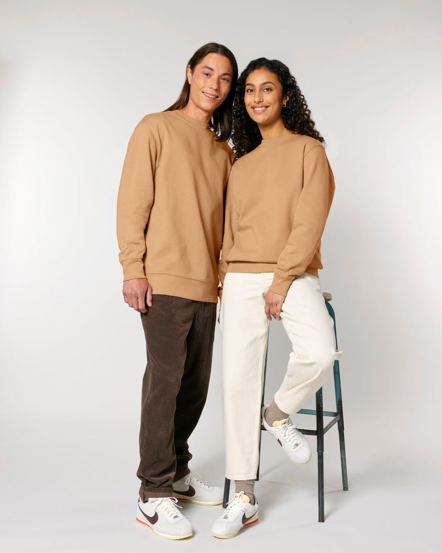 Two individuals posing together, one standing and the other sitting on a stool, both wearing casual attire including the STSU178 Stella/Stella Changer 2.0 The Iconic Unisex Crew Neck Sweatshirt from Stanley/Stella.