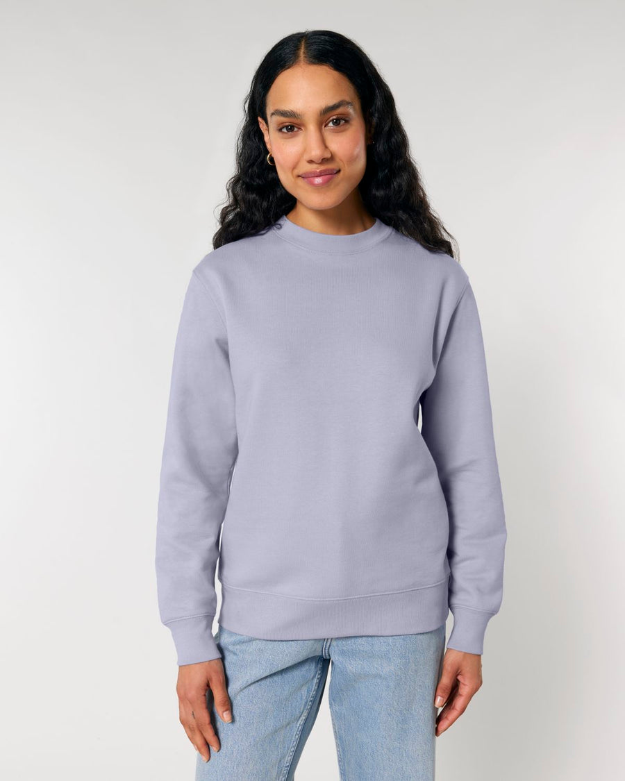 Woman in a STSU178 Stella Changer 2.0 The Iconic Unisex Crew Neck Sweatshirt by Stanley/Stella made of organic cotton and blue jeans standing against a light background.