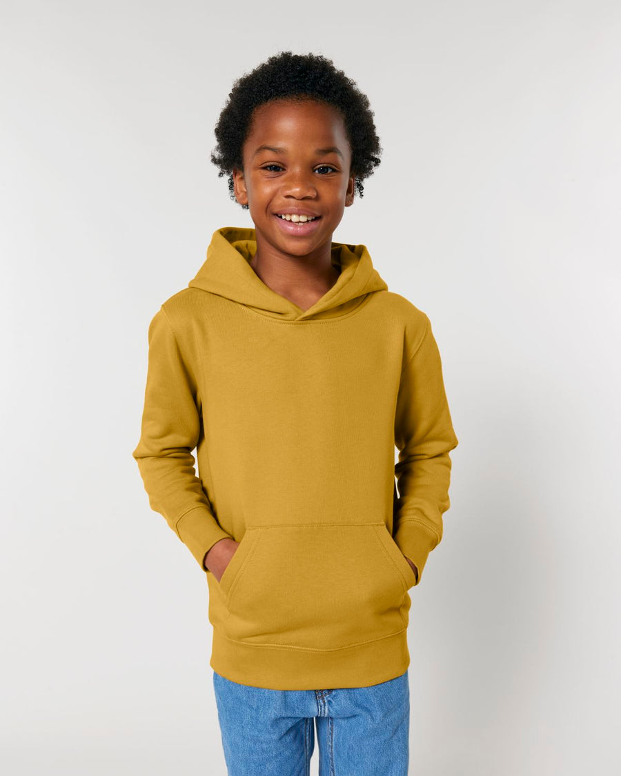 A boy wearing a yellow Stanley/Stella STSK180 Stella Mini Cruiser 2.0 The Iconic Kids Hoodie Sweatshirt.