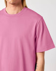 Man wearing a plain pink STTU171 Stanley/Stella Sparker 2.0 The Unisex Heavy T-Shirt with a visible tattoo on his arm.