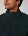 Close-up of a man wearing a dark, water repellent STJM167 Stanley/Stella Navigator Men's Non-Hooded Softshell zip-up jacket with a high collar, focusing on the lower half of his face and the jacket details.