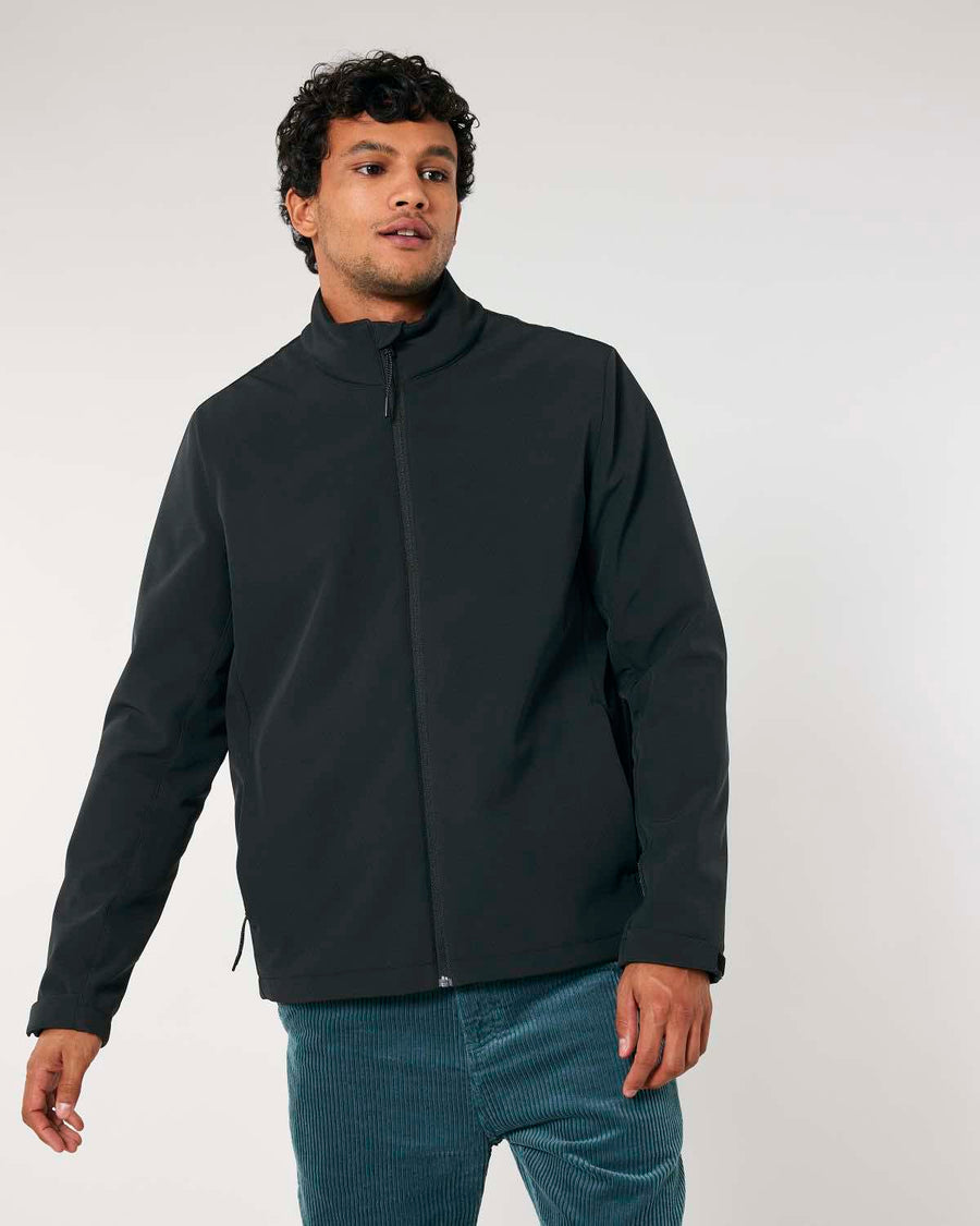 Man in a MyNeedsAreSimple STJM167 Stanley/Stella Navigator Men's Non-Hooded Softshell jacket and teal pants standing against a white background.