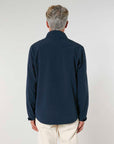 A man standing with his back to the camera, wearing a dark navy MyNeedsAreSimple STJM167 Navigator Men's Non-Hooded Softshell jacket and light beige pants, against a neutral background.