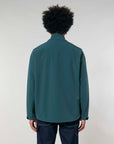 A man with curly hair seen from the back, wearing a MyNeedsAreSimple STJM167 Stanley/Stella Navigator Men's Non-Hooded Softshell jacket in dark teal and blue jeans against a gray background.