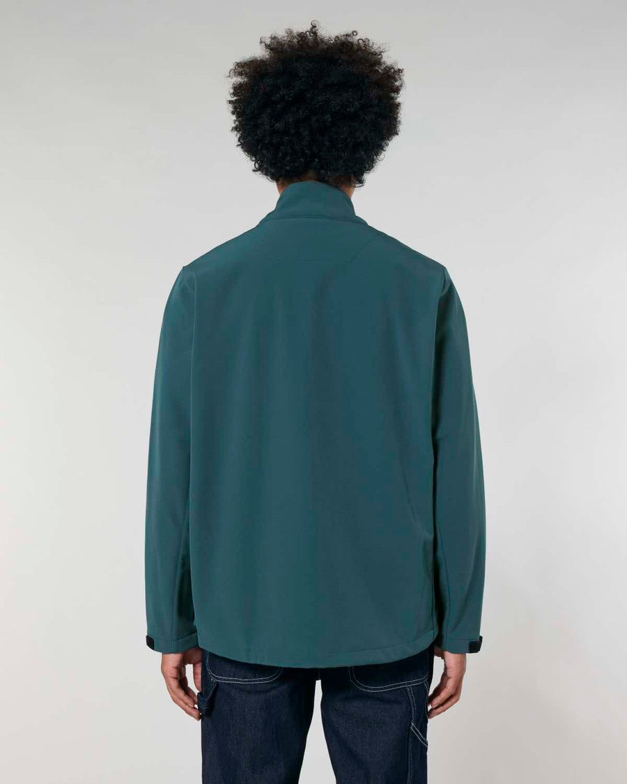 A man with curly hair seen from the back, wearing a MyNeedsAreSimple STJM167 Stanley/Stella Navigator Men's Non-Hooded Softshell jacket in dark teal and blue jeans against a gray background.