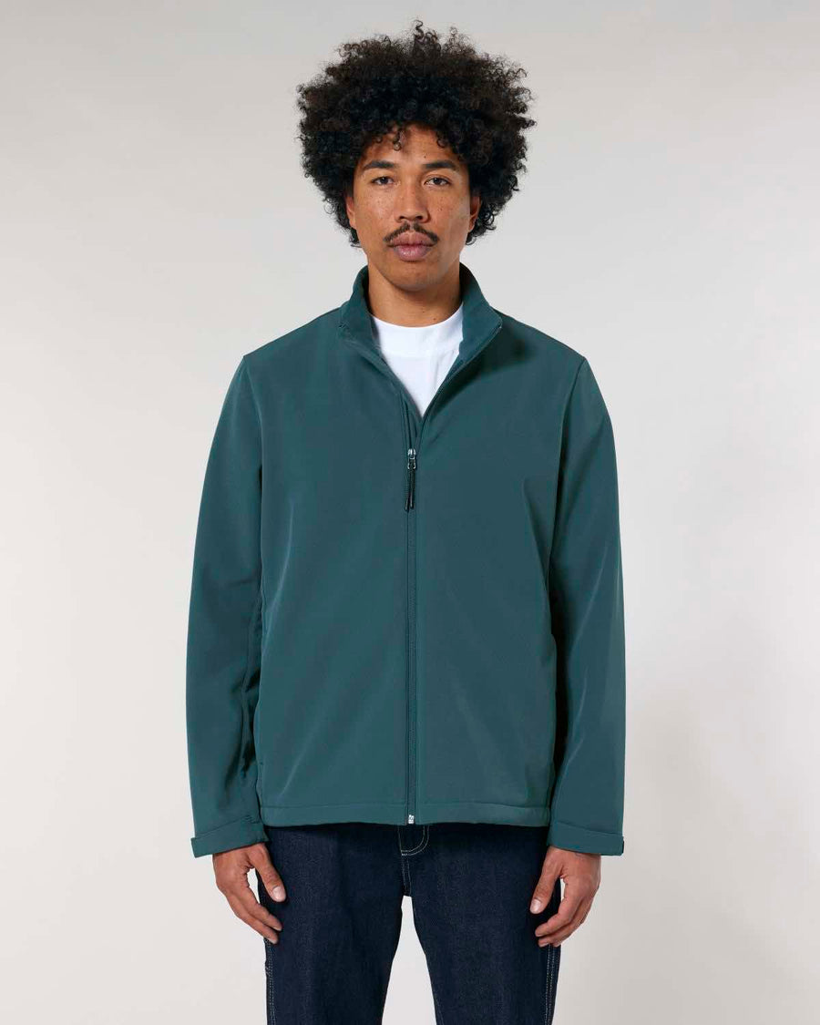 A man with curly hair wears a MyNeedsAreSimple STJM167 Stanley/Stella Navigator Men's Non-Hooded Softshell jacket in green and a white shirt, standing against a neutral background.