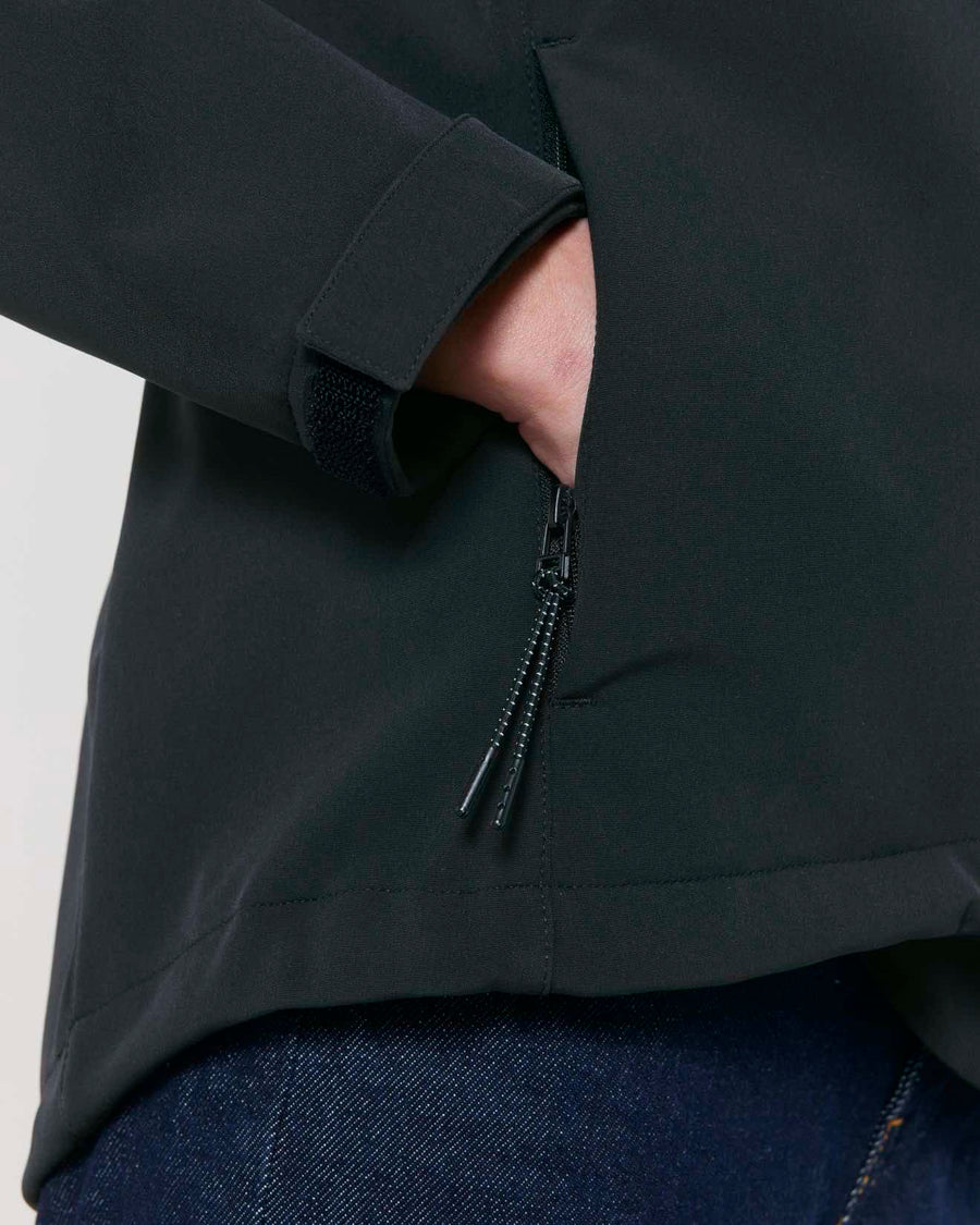 Close-up of a person wearing a MyNeedsAreSimple STJW166 Stanley/Stella Navigator Women's Non-Hooded Softshell black jacket with a zipper pocket on the sleeve, hand partially inserted into the pocket.