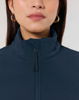Close-up of a woman wearing a MyNeedsAreSimple STJW166 Stanley/Stella Navigator Women’s Non-Hooded Softshell jacket with a high collar and gold hoop earrings.
