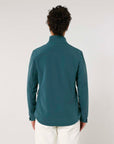 A person viewed from behind wearing a MyNeedsAreSimple STJW166 Stanley/Stella Navigator Women’s Non-Hooded Softshell teal jacket and white pants against a plain background.