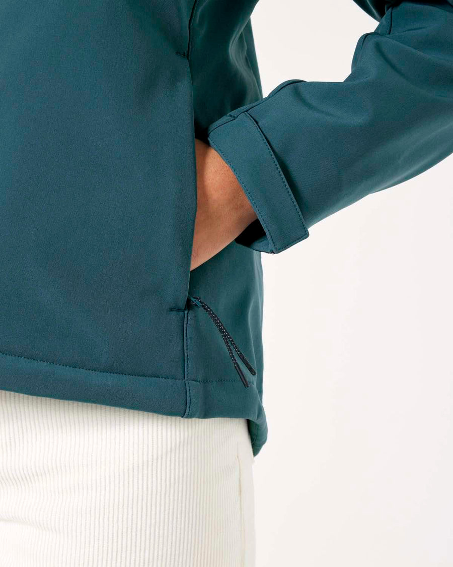 A person wearing a teal, breathable and windproof MyNeedsAreSimple STJW166 Stanley/Stella Navigator Women’s Non-Hooded Softshell jacket with one hand tucked into a pocket, shown against a white background.