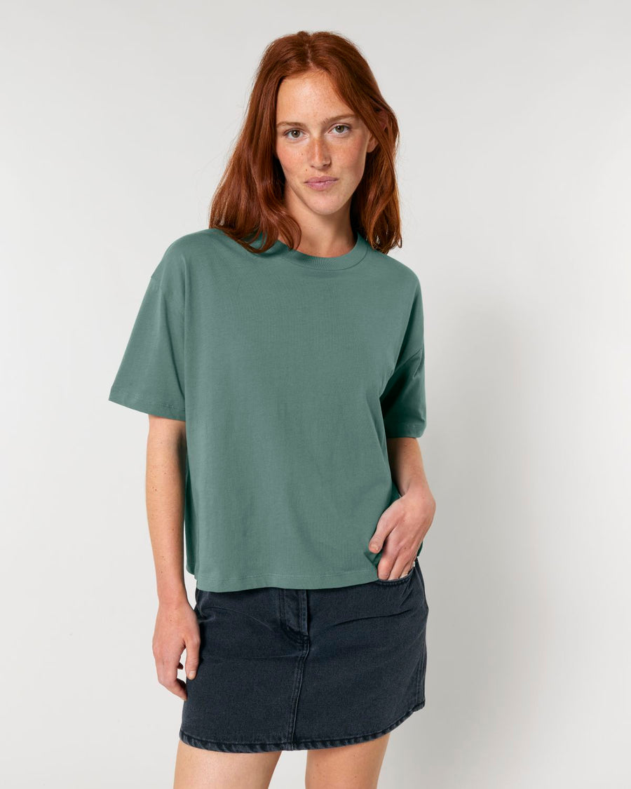 Woman wearing a green STTW175 Stella Nova Womens Boxy T-Shirt and black denim skirt against a white background.