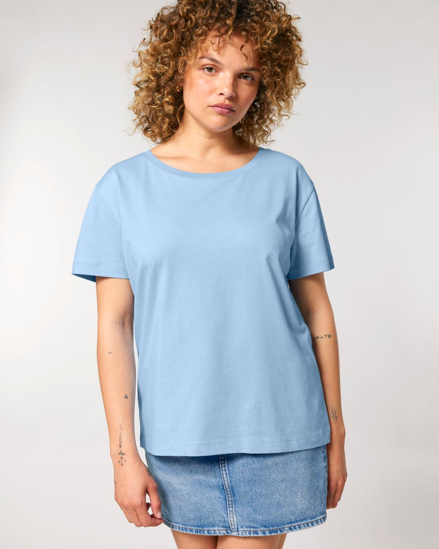 Young woman in a STTW173 Stella Serena Mid-Light Scoop Neck T-shirt and denim skirt standing against a neutral background by Stanley/Stella.