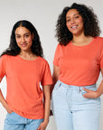 Two smiling women in STTW173 Stella Serena Mid-Light Scoop Neck T-shirts by Stanley/Stella and blue jeans standing side to side.
