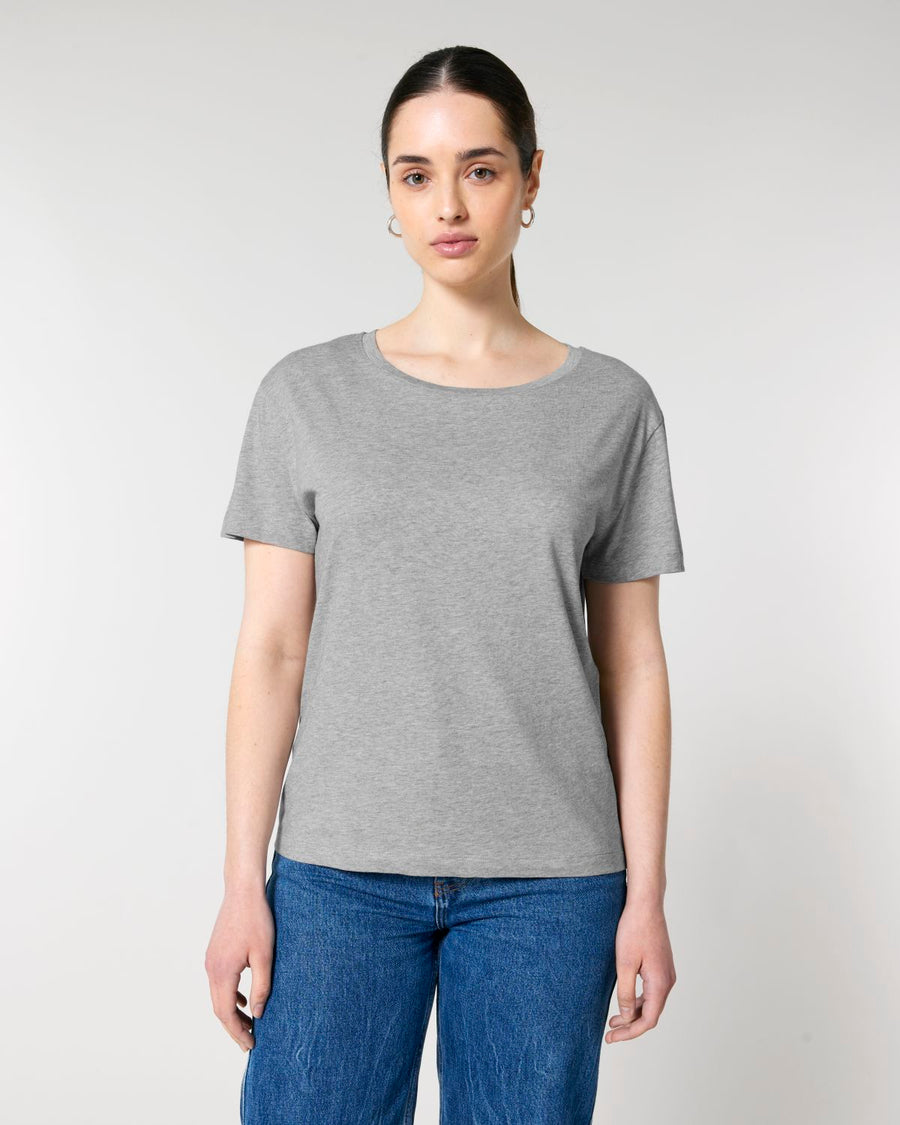 A woman standing against a neutral background, wearing a Stanley/Stella organic plain gray scoop neck t-shirt and blue jeans.