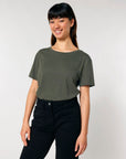 Woman smiling in an STTW173 Stella Serena Mid-Light Scoop Neck T-shirt by Stanley/Stella and black pants against a neutral background.