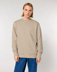 Man wearing a Stanley/Stella organic cotton beige crew neck sweatshirt and blue jeans standing against a white background.