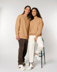 Two people in casual attire, one wearing a Stanley/Stella organic cotton sweatshirt and the other posing for a photo, one standing and one seated on a stool.