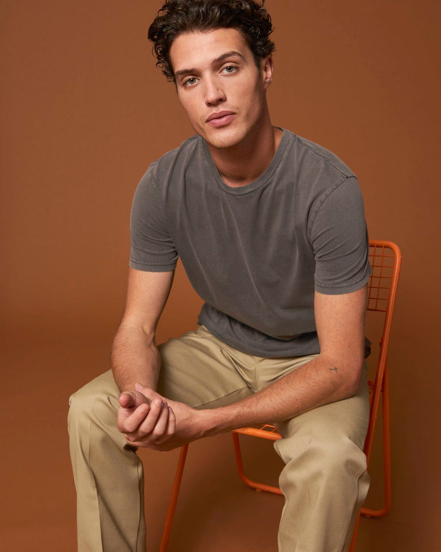 A man sitting on a chair wearing a STTU831 Stanley/Stella Creator Vintage Unisex T-shirt made of organic cotton, paired with khaki pants.