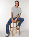 A man sitting on a stool in a grey Stanley/Stella Creator Vintage Unisex T-Shirt and sneakers.