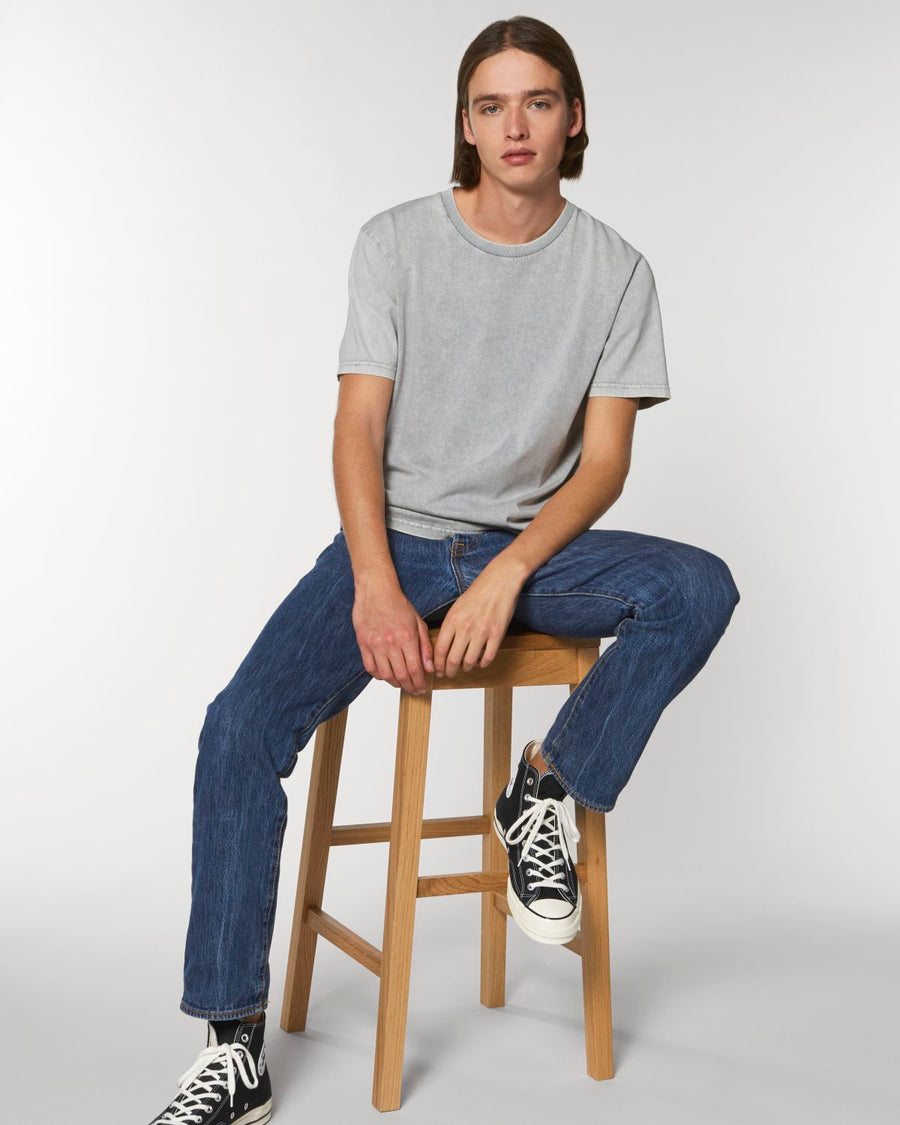 A man sitting on a stool in a grey Stanley/Stella Creator Vintage Unisex T-Shirt and sneakers.