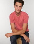 A man wearing a pink Stanley/Stella Creator Vintage Unisex T-Shirt is seated on a wooden stool.