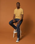 A man in a yellow STTU831 Stanley/Stella Creator Vintage Unisex T-shirt sitting on a stool made of organic cotton.