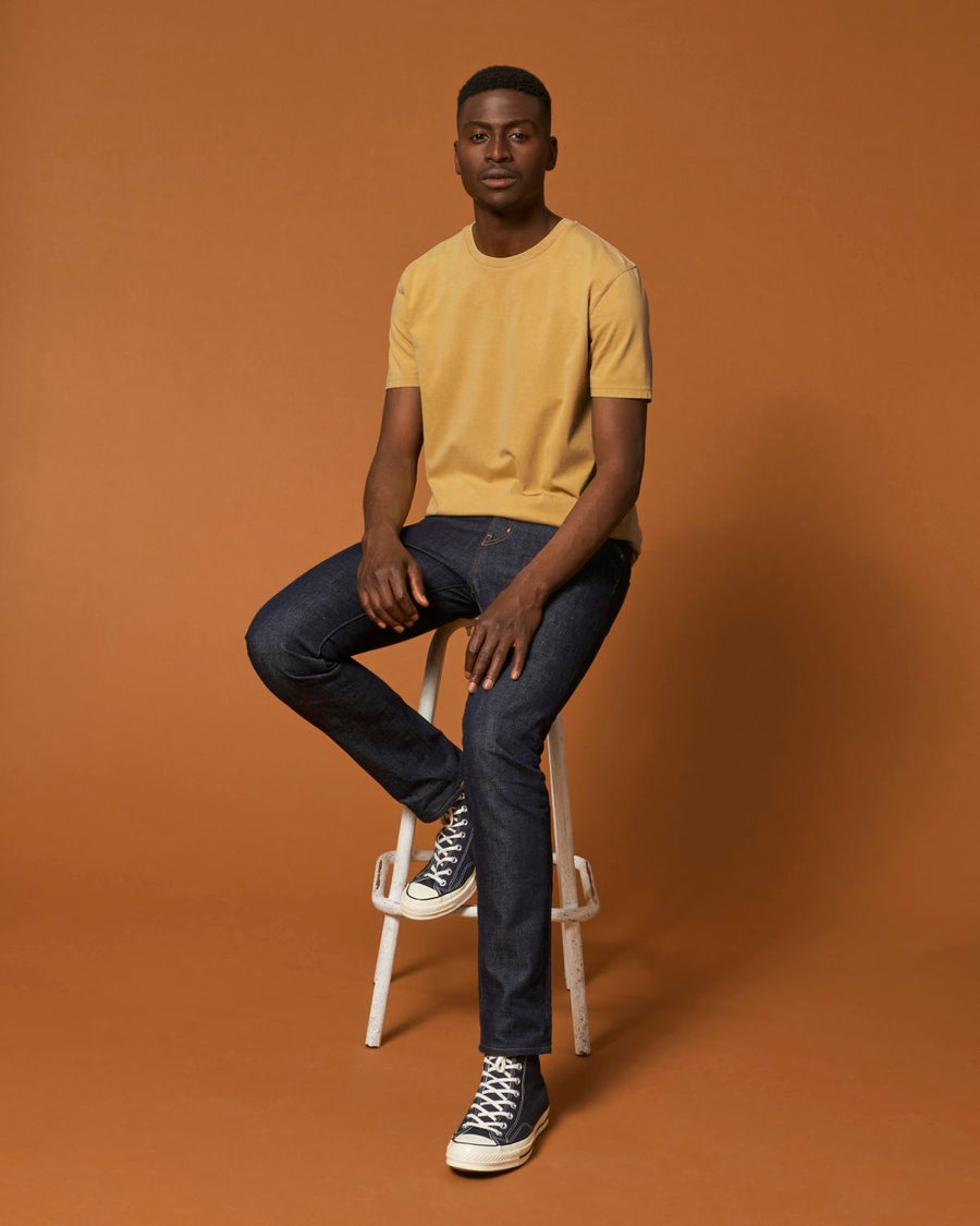 A man in a yellow STTU831 Stanley/Stella Creator Vintage Unisex T-shirt sitting on a stool made of organic cotton.