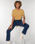 A woman wearing a STTU831 Stanley/Stella Creator Vintage Unisex T-Shirt is sitting on a stool.