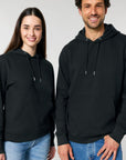 A woman and a man smiling and wearing plain black Stanley/Stella organic cotton hoodies with jeans.